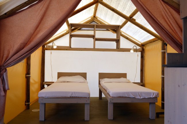 Interno di una tenda con due letti singoli e luci soffuse.