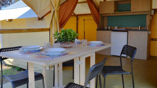 Interno di una tenda glamping con tavolo apparecchiato, sedie nere e angolo cottura.