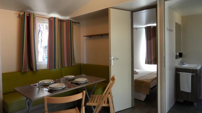 Sala da pranzo con tavolo apparecchiato e sedie pieghevoli, porta aperta su camera da letto.