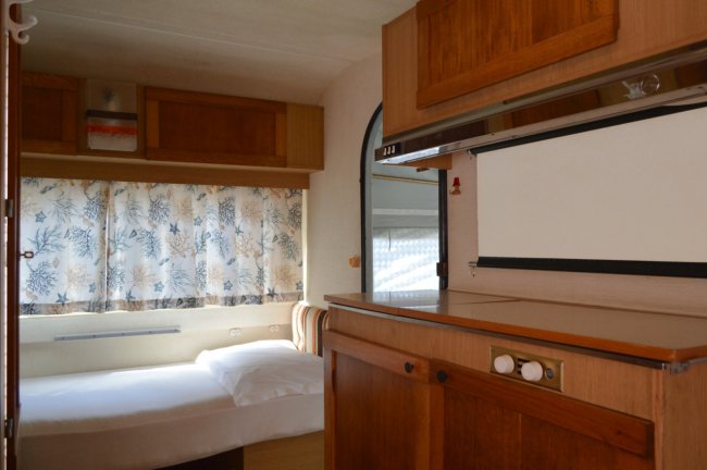 Camera con letto singolo e armadietti in legno, finestra con tende floreali.