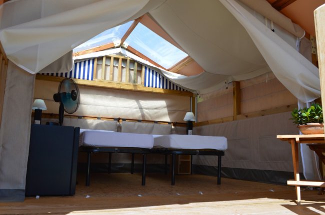 Interno di una tenda glamping con due letti singoli, ventilatore e lucernario.