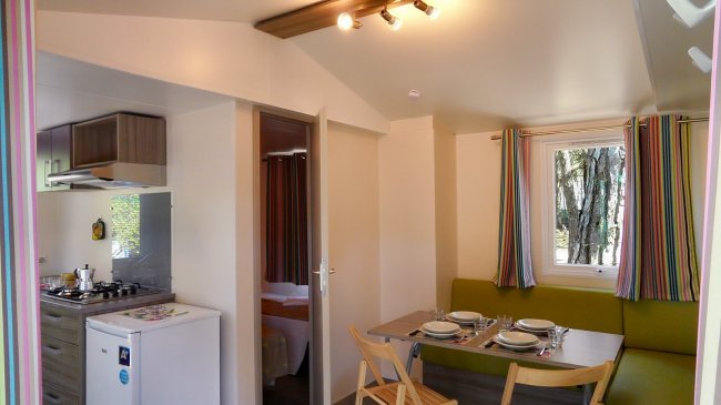 Interno di una casa mobile con cucina attrezzata, tavolo da pranzo e salottino verde.