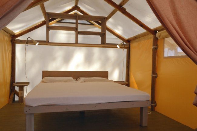 Tenda glamping con letto matrimoniale, illuminazione e struttura in legno.