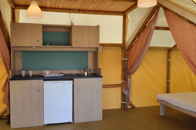 Interno di una tenda con cucina in legno, mini frigorifero e letto.