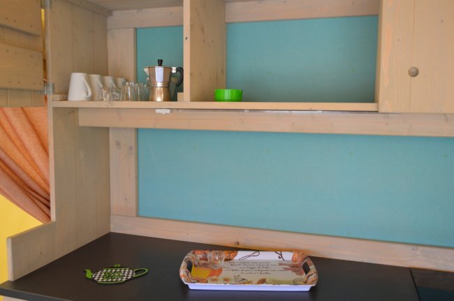 Mensola di cucina con tazze, bicchieri, una caffettiera e un vassoio su un piano di lavoro.