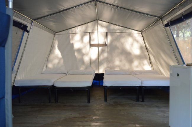 Interno di una tenda con quattro letti singoli su pavimento in legno.