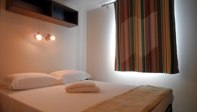 Camera con letto matrimoniale, mensola, tende a righe e lampade da parete.