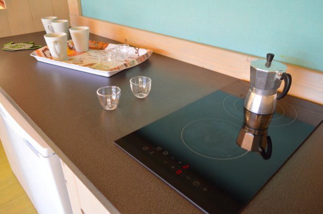 Piano cucina con fornello a induzione, caffettiera, tazzine e vassoio.