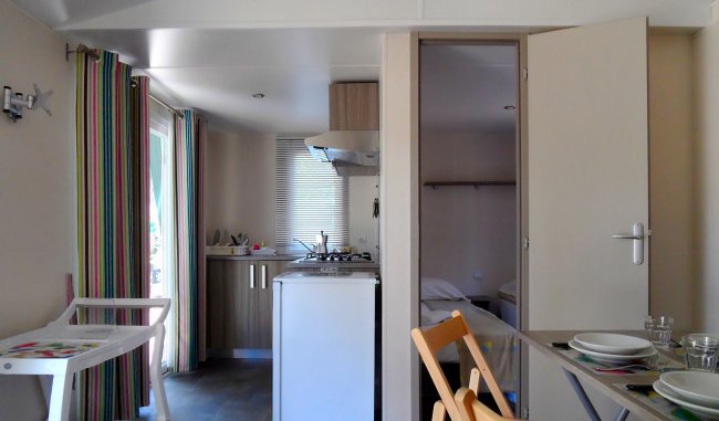 Interno compatto con cucina, tavolo apparecchiato e porta aperta verso una camera.