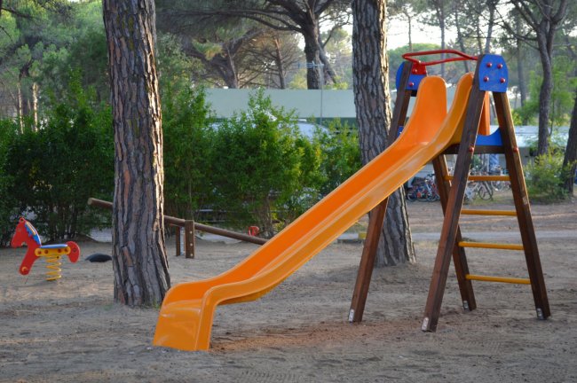 Uno scivolo arancione con scala in un parco giochi tra gli alberi.