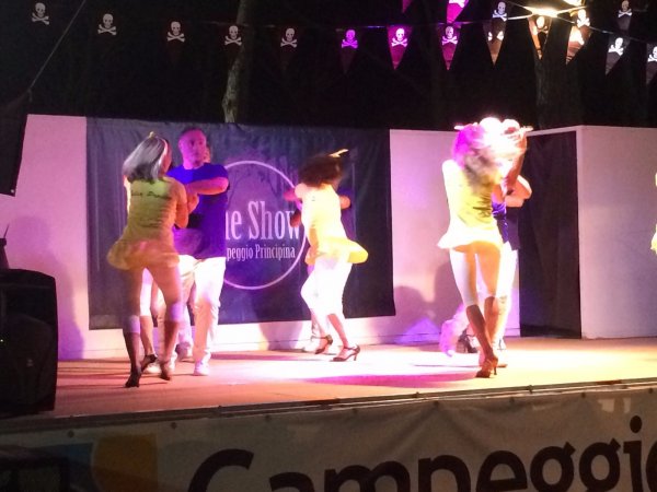 Persone su un palco ballano con illuminazione colorata.