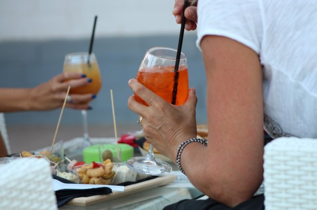 Due persone tengono cocktail arancioni e bianchi su un tavolino con stuzzichini.