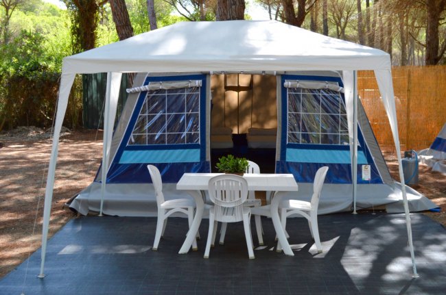 Una tenda blu con un gazebo bianco e un tavolo con sedie di plastica all'aperto.