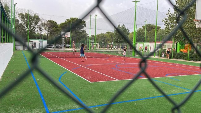 Persone giocano a tennis su campo recintato.