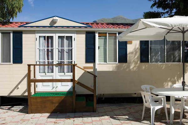 Casa mobile con terrazza, ombrellone e sedie su un patio.