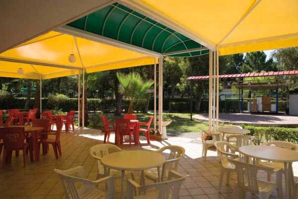 Tavolini e sedie di plastica sotto un tendone giallo in un'area esterna coperta.