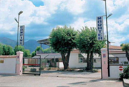 Ingresso di un campeggio con cancello e due alberi.