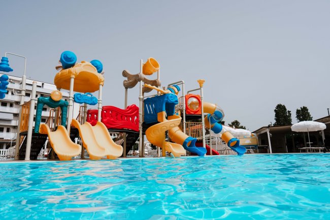 Parco acquatico con scivoli gialli e arancioni, giochi d'acqua blu e rossi, immerso in una piscina.