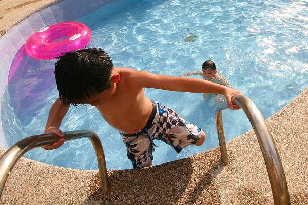 Un bambino sale le scale fuori da una piscina, mentre un altro nuota vicino a un gonfiabile rosa.