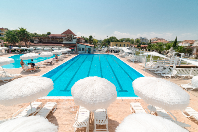 Ampia piscina blu con ombrelloni bianchi e lettini intorno, cielo sereno.