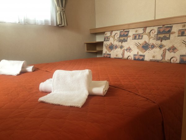 Letto matrimoniale con copriletto arancione e asciugamani bianchi piegati sopra.