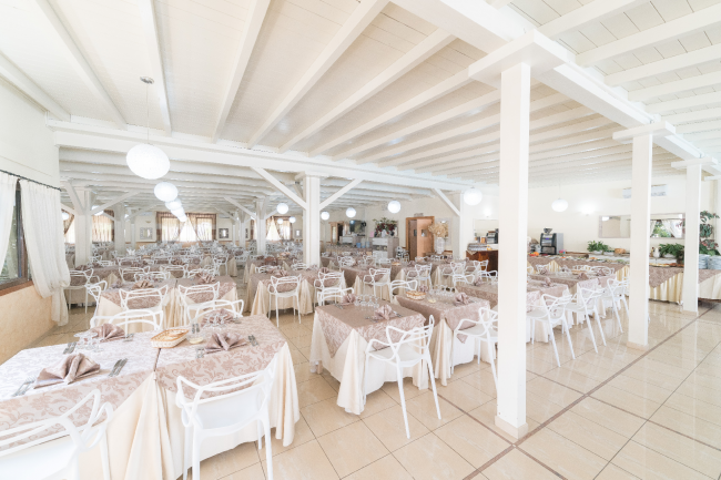 Sala da pranzo ampia con tavoli apparecchiati e sedie bianche.