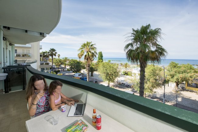 Due persone su un balcone con vista mare e palme.