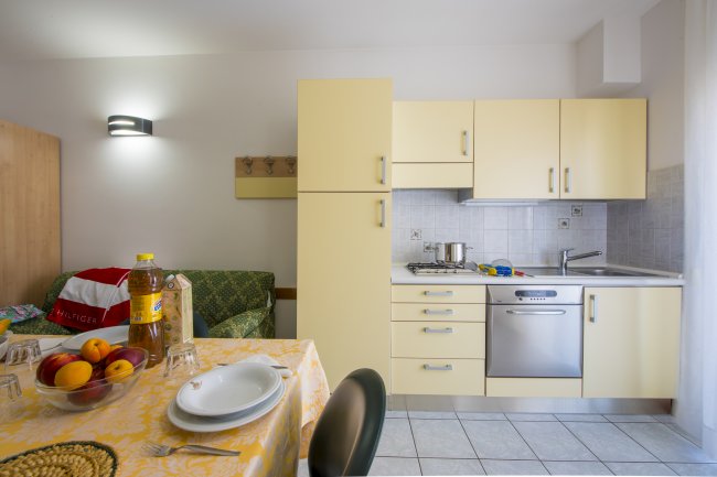 Cucina moderna con mobili gialli, tavolo apparecchiato e divano con cuscini colorati.