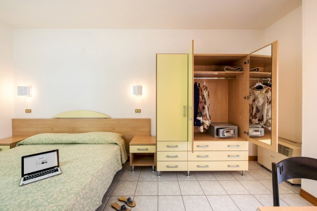 Camera da letto con letto matrimoniale, armadio aperto, portatile sul letto e vestiti appesi.