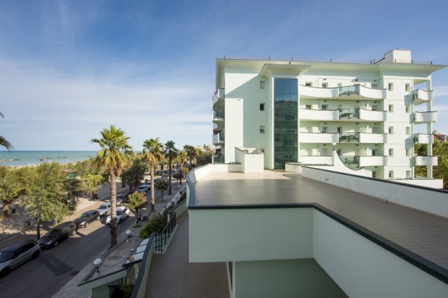 Edificio moderno vicino al mare, circondato da palme sotto un cielo sereno.