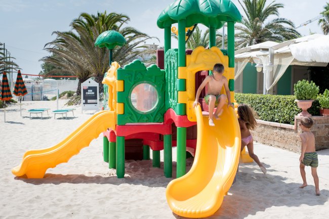 Bambini giocano su uno scivolo colorato su una spiaggia.