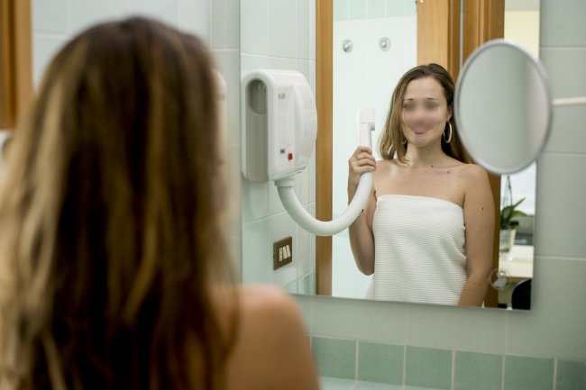 Donna usa un asciugacapelli in bagno, guardando lo specchio.