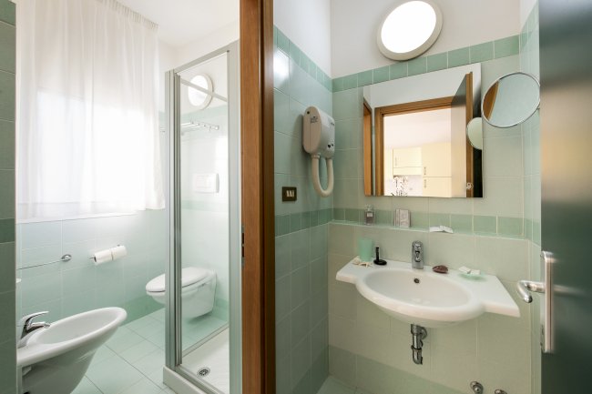 Bagno luminoso con doccia, lavabo e WC. Piastrelle color menta e specchio sopra il lavabo.