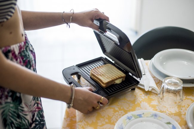 Persona che prepara un toast in una macchina per panini su una tavola apparecchiata.