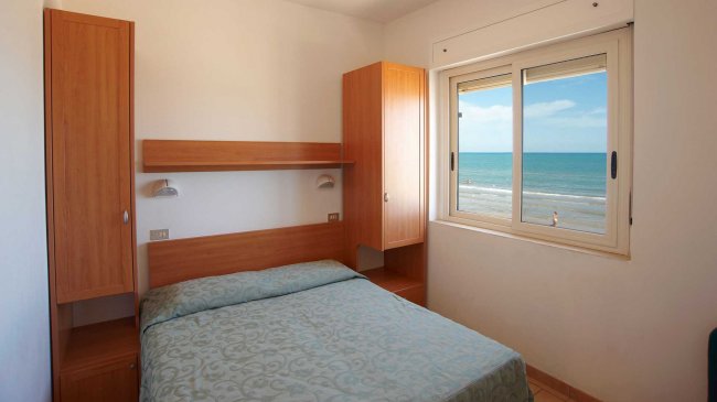 Camera da letto con finestra vista mare, letto matrimoniale e mobili in legno chiaro.