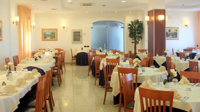 Sala da pranzo raffinata con tavoli rotondi e sedie in legno, decorata con fiori.