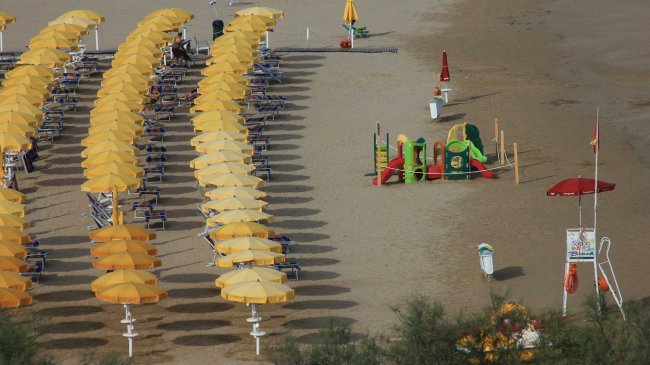 Spiaggia con file di ombrelloni gialli e un'area giochi per bambini.