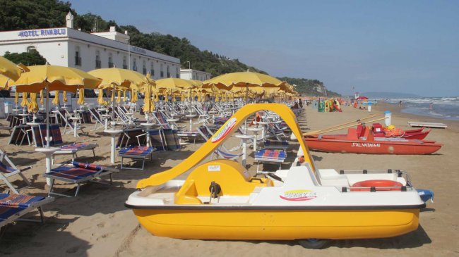 Spiaggia con sdraio e ombrelloni gialli sotto un cielo sereno.