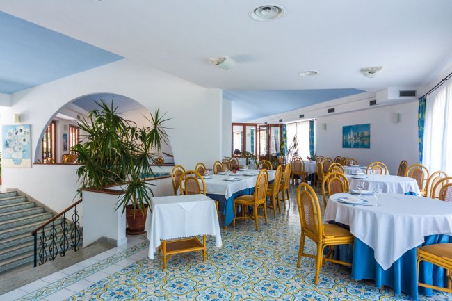 Ristorante luminoso con tavoli apparecchiati e sedie, pavimento decorato a motivi geometrici.