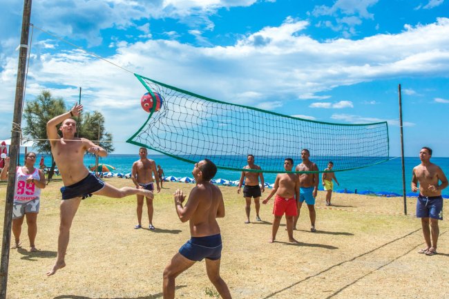 Persone giocano a beach volley su un prato vicino al mare. Cielo azzurro.