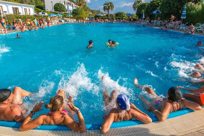 Persone in piscina fanno esercizi con schizzi d'acqua, mentre altre nuotano.