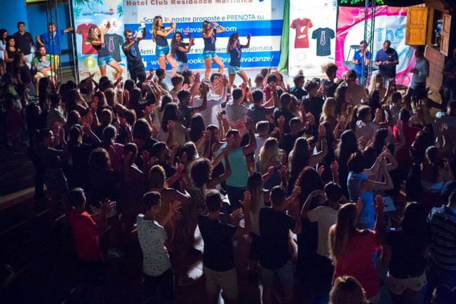 Festa con una folla che balla davanti a un palco in un ambiente notturno.
