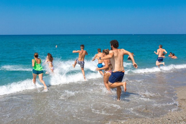 Persone corrono verso il mare turchese sulla spiaggia.