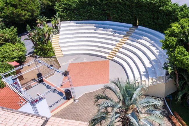 Anfiteatro all'aperto con gradinate semicircolari, circondato da vegetazione.