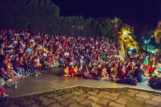 Grande folla riunita su gradinate all'aperto di notte, circondata da palme.