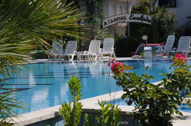 Piscina con sdraio bianche e ingresso con insegna 