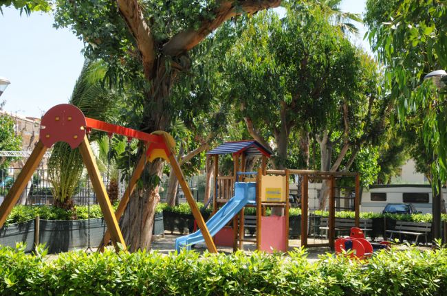 Parco giochi con altalena e scivolo colorato tra gli alberi.