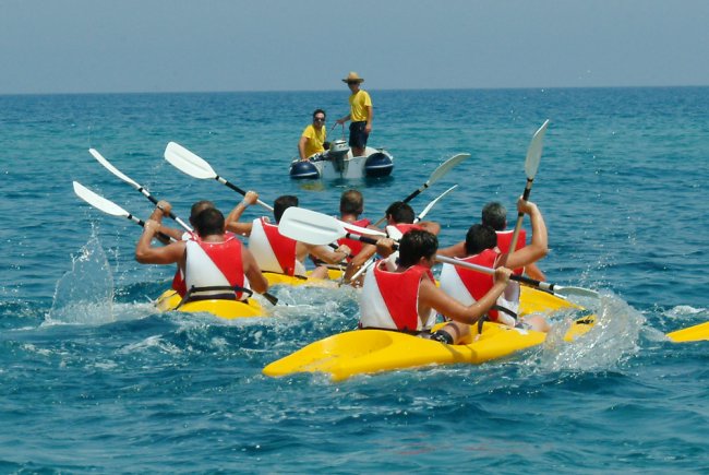 Persone in kayak gialli con giubbotti rossi pagaiando nel mare blu.