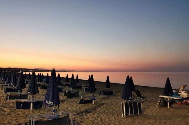 Spiaggia al tramonto con ombrelloni chiusi.