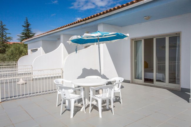Una terrazza con tavolo e sedie bianche sotto un ombrellone blu e bianco.